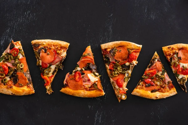 Vue de dessus de délicieuses tranches de pizza italienne avec des légumes et du salami sur fond noir — Photo de stock