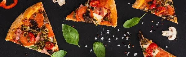 Vista superior de deliciosas rebanadas de pizza italiana con verduras y salami sobre fondo negro, plano panorámico - foto de stock