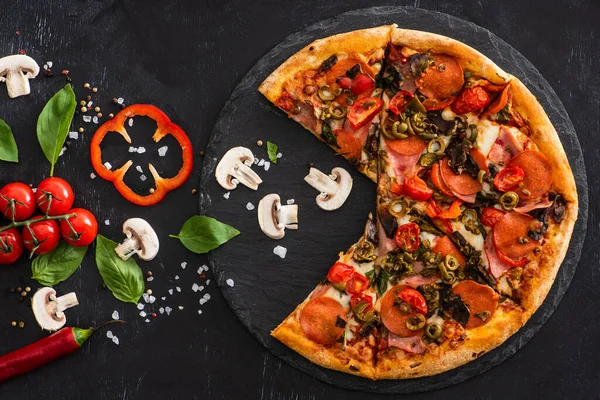 Draufsicht auf köstliche italienische Pizza mit Gemüse und Salami auf schwarzem Hintergrund — Stockfoto
