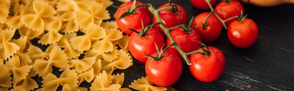 Farfalle italiane crude con pomodori su fondo nero, colpo panoramico — Foto stock