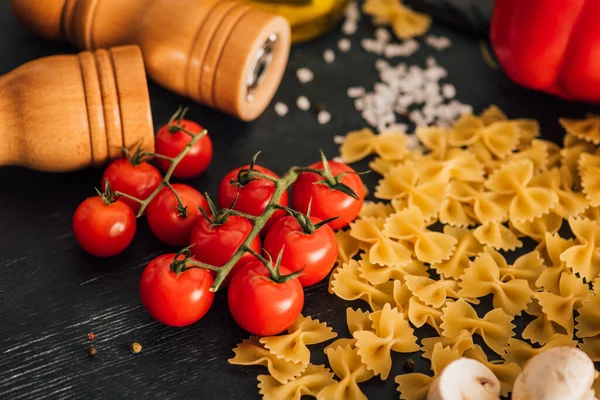 Raw Italian farfalle with tomatoes and salt on black background — Stock Photo