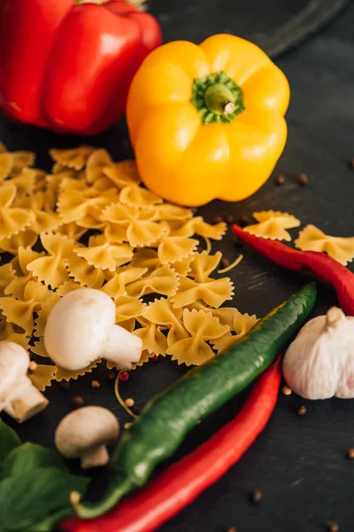 Raw Italian farfalle with vegetables on black background — Stock Photo