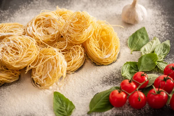 Capellini italiano crudo con verduras y harina sobre fondo negro - foto de stock