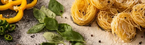 Capellini crudi italiani con verdure su farina su fondo nero, colpo panoramico — Foto stock