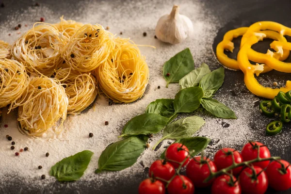 Capellini italiano crudo con verduras sobre harina sobre fondo negro - foto de stock