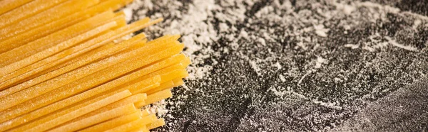 Vista de perto de espaguete cru e farinha no fundo preto, tiro panorâmico — Fotografia de Stock