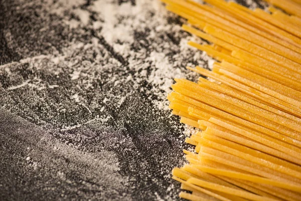Vista de perto de espaguete cru e farinha no fundo preto — Fotografia de Stock