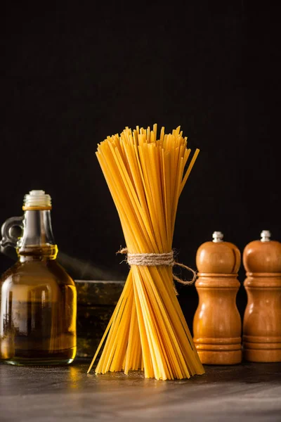 Uncooked Italian spaghetti with olive oil and condiments isolated on black — Stock Photo