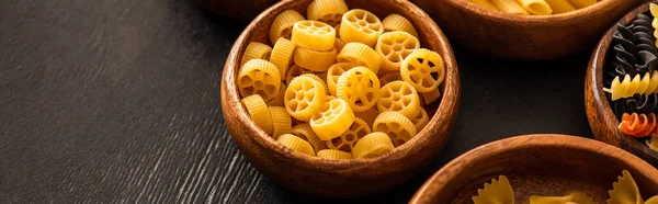 Raw Italian Rotelle pasta in wooden bowl on black background, panoramic shot — Stock Photo