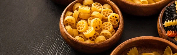 Pasta Rotelle italiana cruda en cuenco de madera sobre fondo negro, plano panorámico - foto de stock