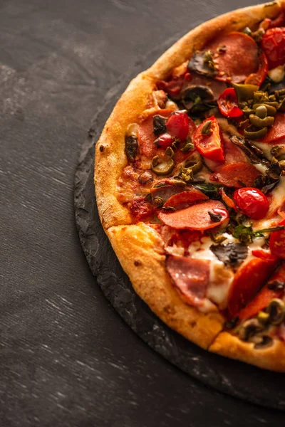 Top view of delicious Italian pizza with vegetables and salami on black wooden background — Stock Photo