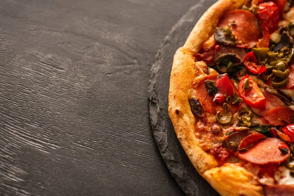 Top view of delicious Italian pizza with vegetables and salami on black wooden background — Stock Photo