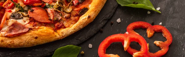Vista de cerca de la deliciosa pizza italiana con salami cerca de verduras sobre fondo negro, plano panorámico - foto de stock