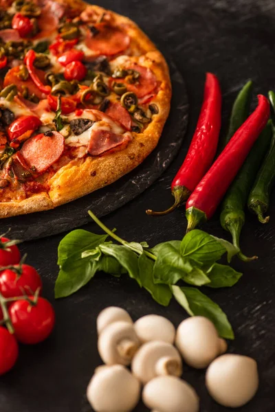 Foco seletivo de deliciosa pizza italiana com salame perto de legumes em fundo preto — Fotografia de Stock