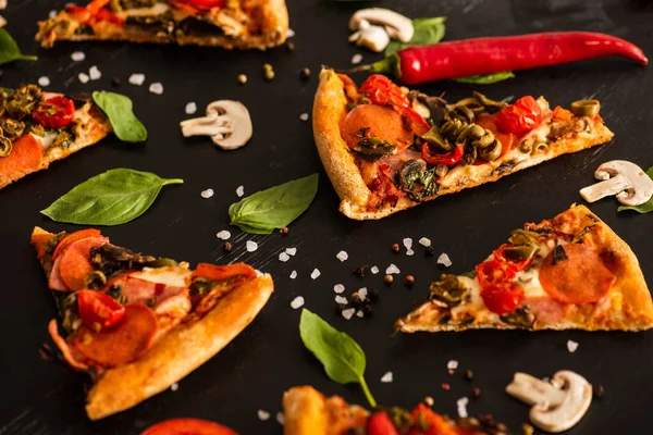 Foco seletivo de deliciosas fatias de pizza italiana com salame perto de legumes no fundo preto — Fotografia de Stock