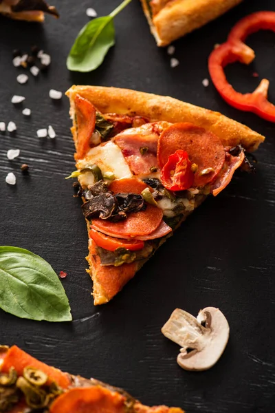 Delicious Italian pizza slice with salami near vegetables on black background — Stock Photo