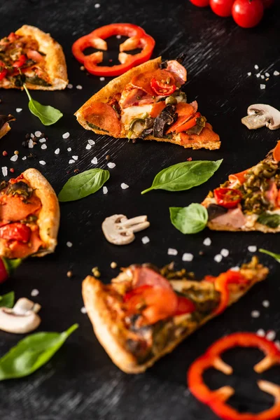 Selective focus of delicious Italian pizza slices with salami near vegetables on black background — Stock Photo