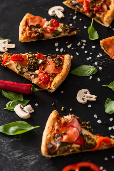 Enfoque selectivo de deliciosas rebanadas de pizza italiana con salami cerca de verduras sobre fondo negro - foto de stock