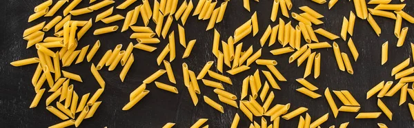 Top view of raw penne pasta scattered on black background, panoramic shot — Stock Photo