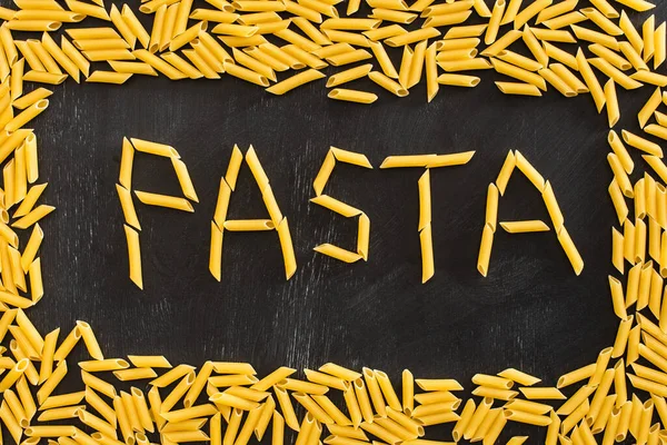 Top view of pasta word made of raw penne on black background — Stock Photo