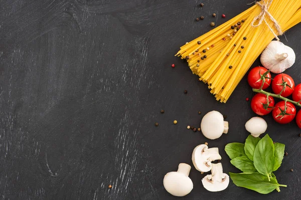 Draufsicht auf rohe italienische Spaghetti mit Gemüse und Gewürzen auf schwarzem Hintergrund — Stockfoto