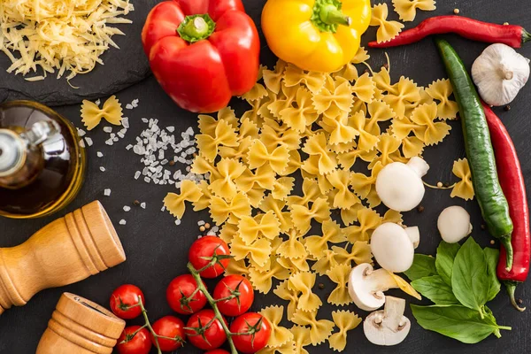 Top view of raw Italian farfalle with vegetables and seasoning on black background — Stock Photo