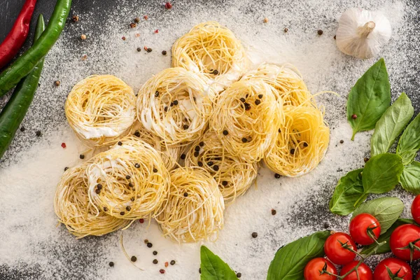 Von oben auf rohe Capellini-Pasta mit Gemüse, Gewürzen und Mehl — Stockfoto