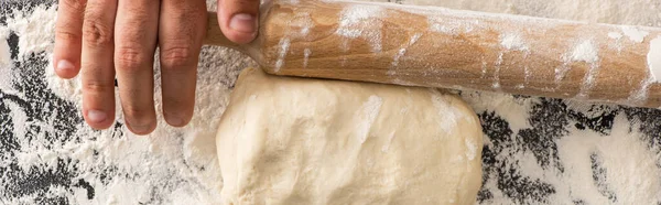 Cropped view of man rolling out dough on flour on black background — Stock Photo