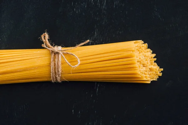 Top view of raw Italian spaghetti tied with string on black background — Stock Photo