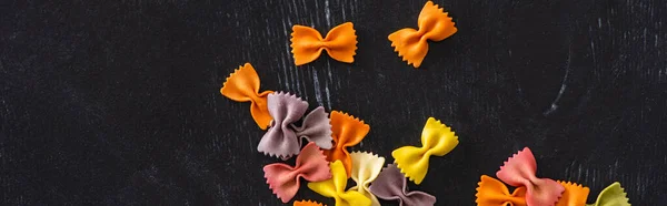 Vue de dessus de pâtes farfalle crues colorées sur fond de bois noir, panoramique — Photo de stock