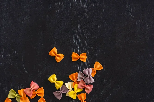 Draufsicht auf bunte rohe Farfalle-Pasta auf schwarzem Holzhintergrund — Stockfoto