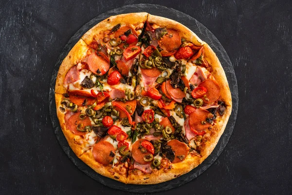 Top view of delicious Italian pizza with salami on black wooden background — Stock Photo