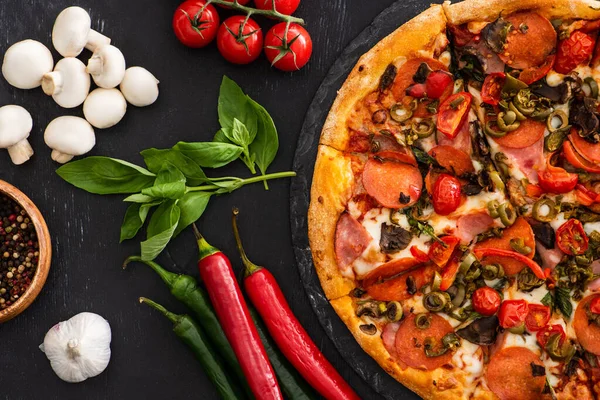 Draufsicht auf köstliche italienische Pizza mit Gemüse und Salami auf schwarzem Hintergrund — Stockfoto