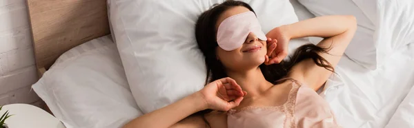 Панорамне поняття молодої жінки в масці для очей, що лежить на ліжку — стокове фото
