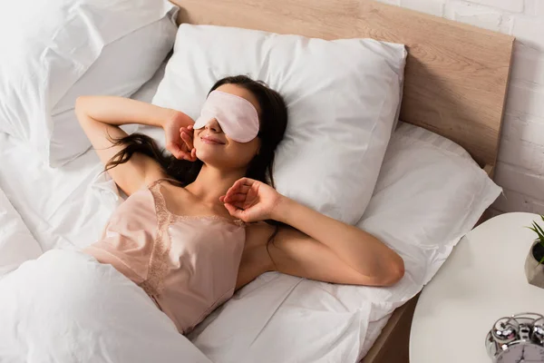 Visão de alto ângulo da jovem mulher na máscara de olho deitado na cama — Fotografia de Stock