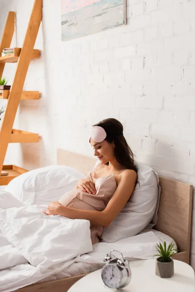 Selective focus of pregnant woman in silk nightie touching belly in bedroom — Stock Photo