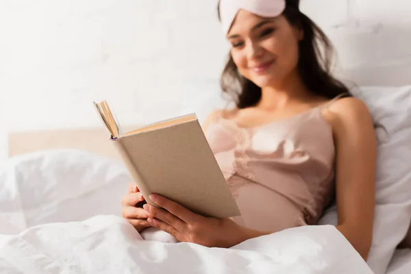 Messa a fuoco selettiva di incinta giovane donna lettura libro in camera da letto — Foto stock