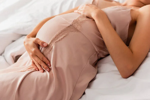 Teilbild einer schwangeren Frau, die auf dem Bett liegt und Bauch berührt — Stockfoto