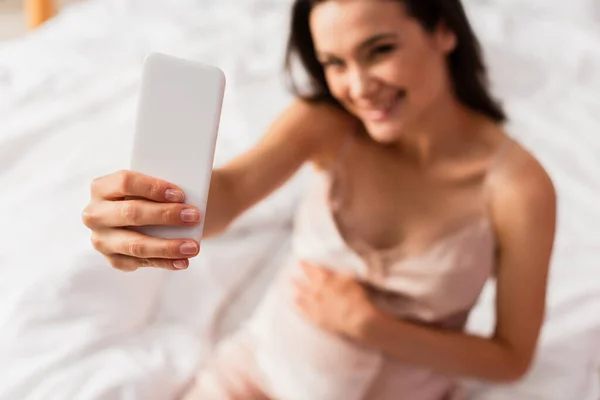 Enfoque selectivo de la mujer embarazada tomando selfie en el dormitorio - foto de stock