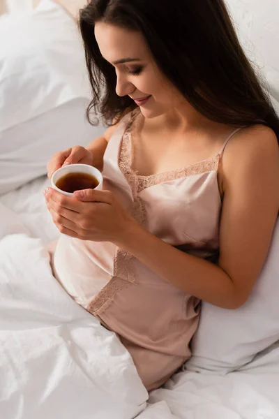 Jeune femme enceinte en chemise de nuit en soie tenant une tasse de thé — Photo de stock