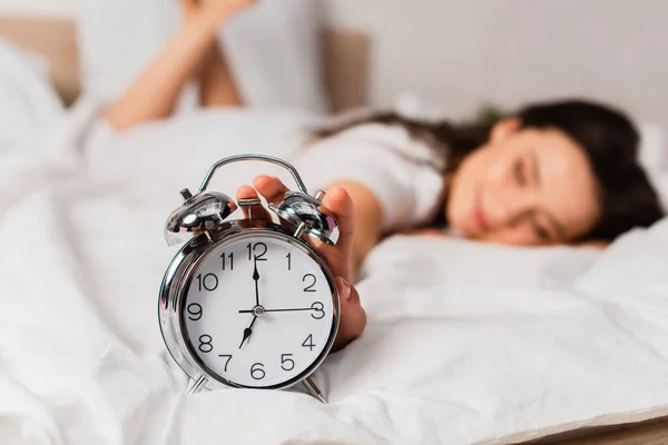 Selective focus of woman lying on bed and reaching retro alarm clock — Stock Photo