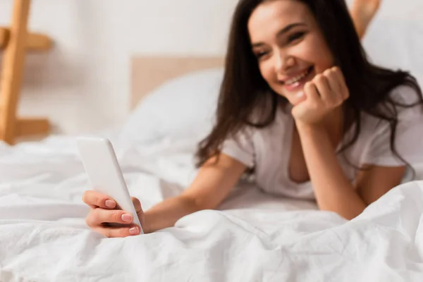 Селективное внимание молодой женщины, лежащей на кровати и использующей смартфон — стоковое фото