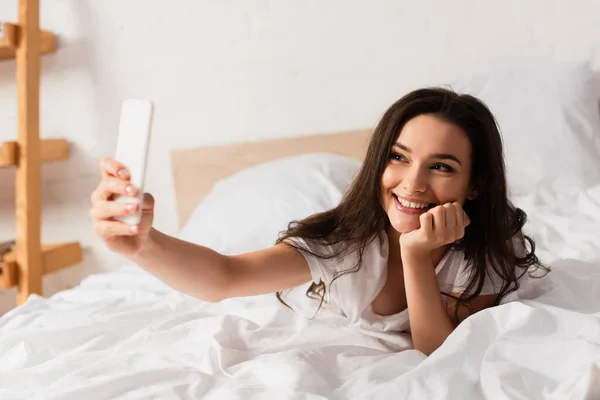 Selective focus of young woman lying on bed and taking selfie — Stock Photo