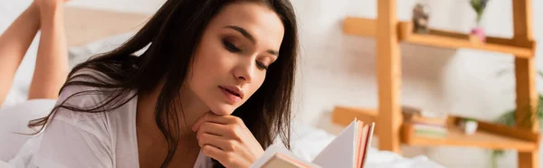 Plano panorámico de mujer morena leyendo libro en el dormitorio - foto de stock