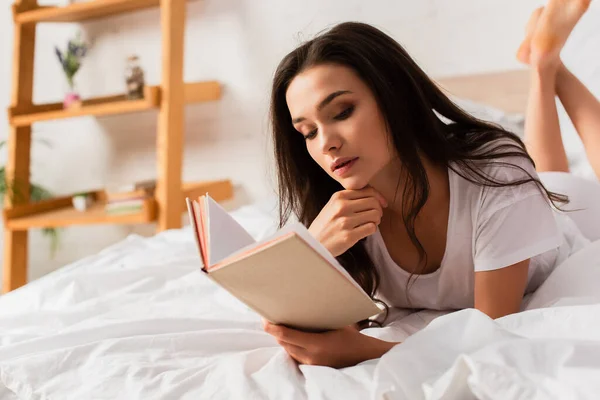 Брюнетка молодая женщина читает книгу и лежит на кровати — стоковое фото