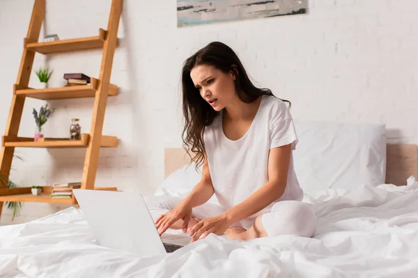 Young and worried freelancer using laptop in bedroom — Stock Photo