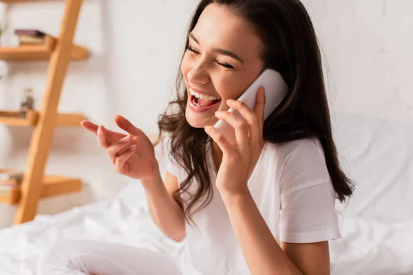 Morena mujer hablando en smartphone mientras gesticulando en el dormitorio - foto de stock