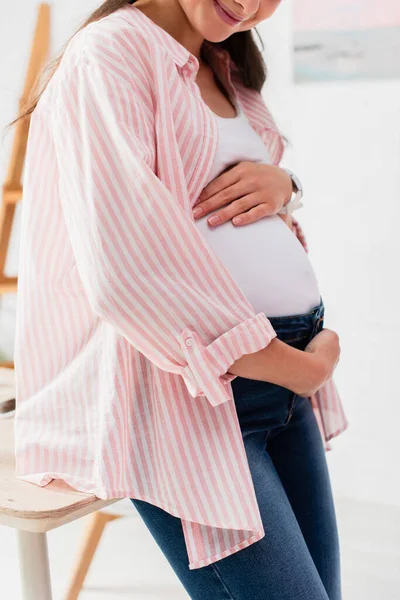 Обрезанный вид беременной женщины, трогающей животик дома — стоковое фото