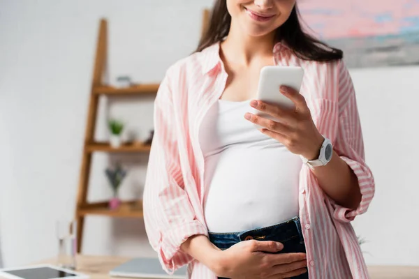 Vue recadrée de la femme enceinte touchant le ventre et utilisant un smartphone — Photo de stock