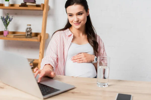 Enfoque selectivo de la mujer embarazada usando el ordenador portátil mientras trabaja desde casa - foto de stock